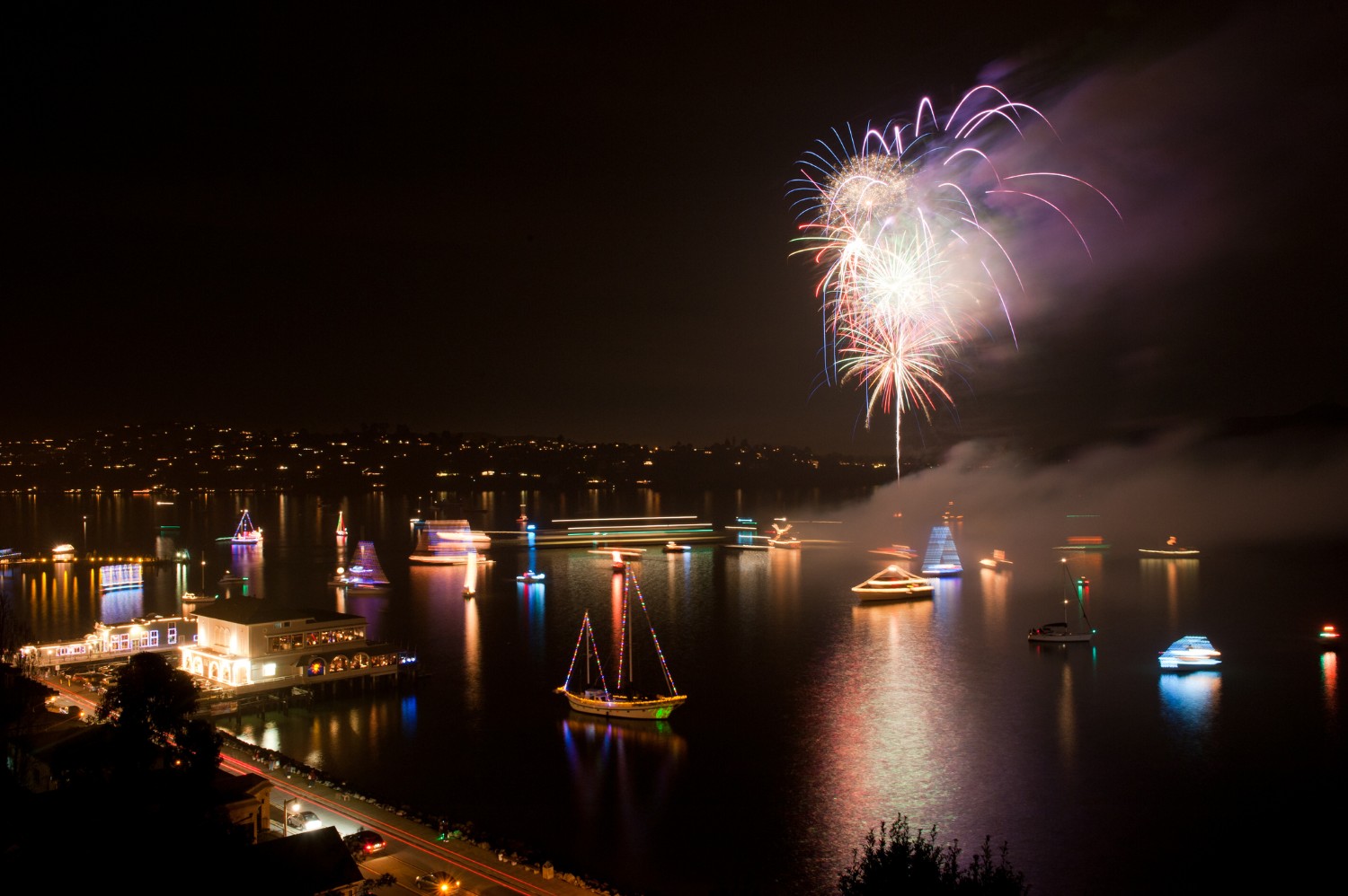 Boats with lights on them and fireworks in the sky