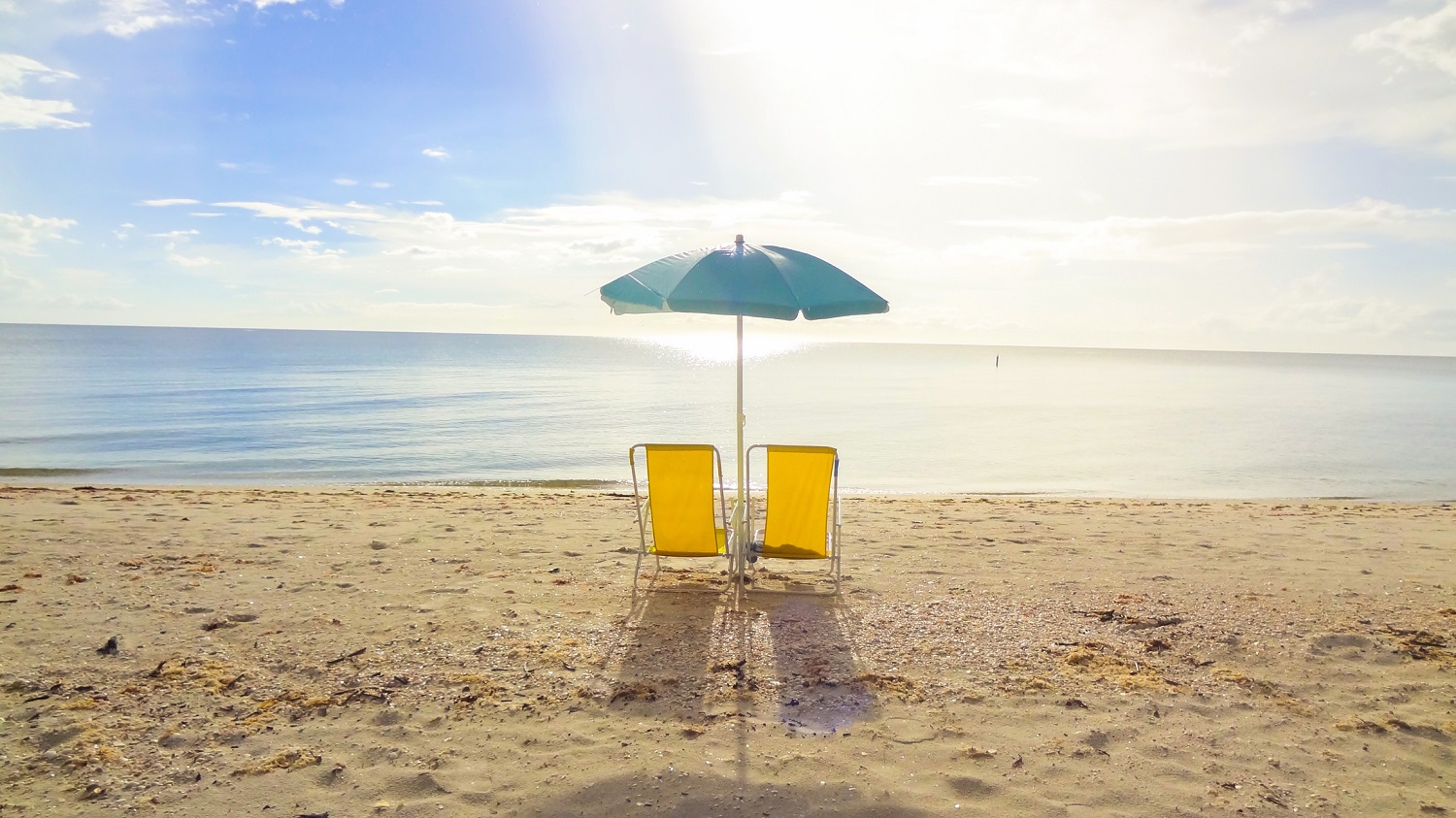 two yellow beach chairs and blue umbrella on the beach